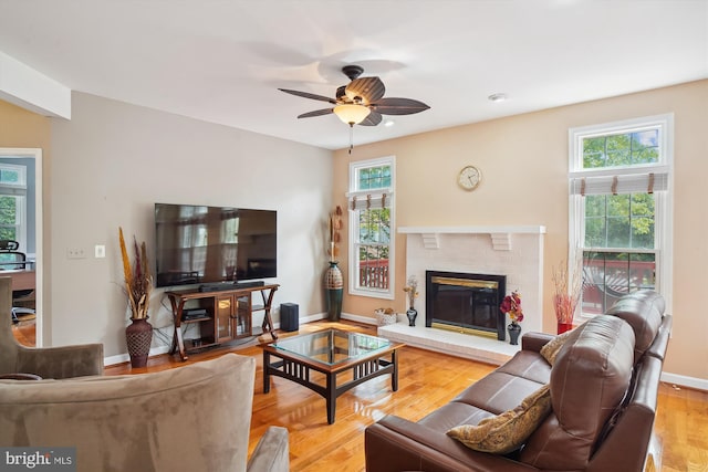 living room with light wood-style floors, a brick fireplace, baseboards, and a ceiling fan