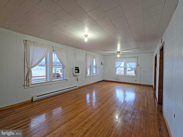 spare room featuring heating unit, baseboard heating, wooden walls, ceiling fan, and hardwood / wood-style flooring