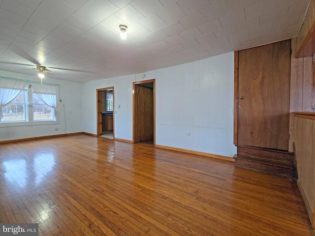 empty room featuring hardwood / wood-style floors, ceiling fan, and wood walls