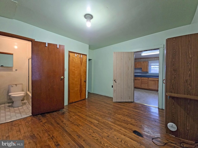 unfurnished bedroom with lofted ceiling, ensuite bathroom, and dark hardwood / wood-style floors