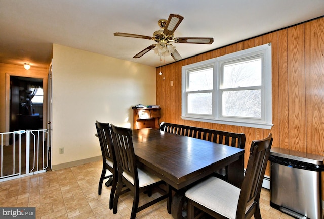 dining area featuring ceiling fan, wooden walls, and a baseboard heating unit