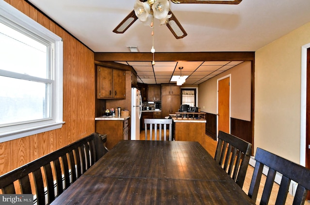 unfurnished dining area featuring wood walls, beamed ceiling, and ceiling fan