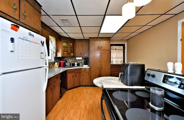 kitchen featuring a paneled ceiling, black appliances, hanging light fixtures, light hardwood / wood-style flooring, and tasteful backsplash