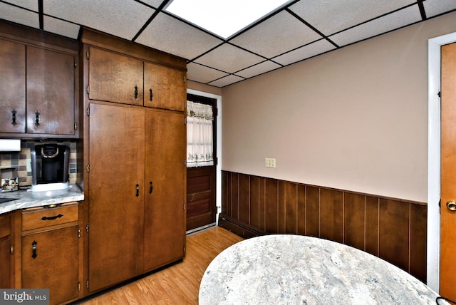 kitchen featuring a paneled ceiling, light hardwood / wood-style floors, wooden walls, and tasteful backsplash