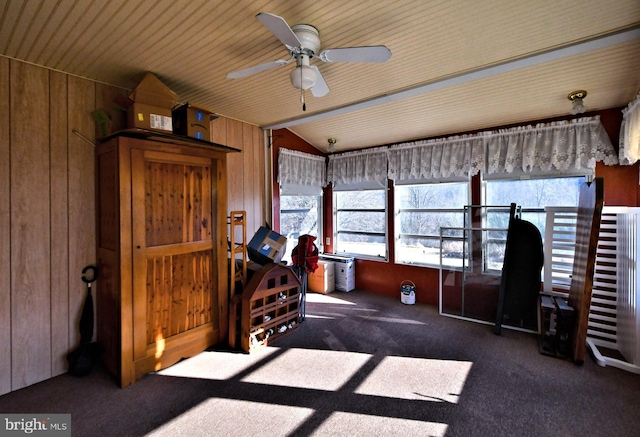 misc room with dark colored carpet, vaulted ceiling, ceiling fan, and wooden walls