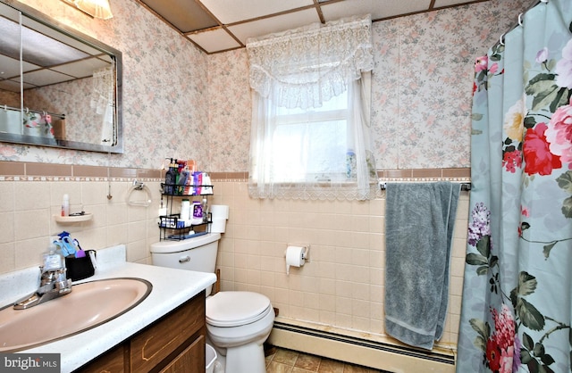 bathroom with vanity, a drop ceiling, toilet, baseboard heating, and tile walls