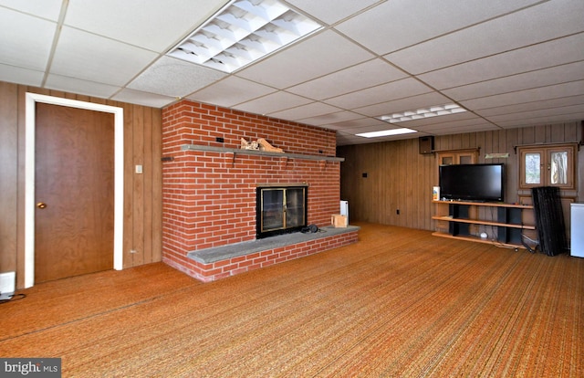 unfurnished living room with a fireplace, wooden walls, and a drop ceiling