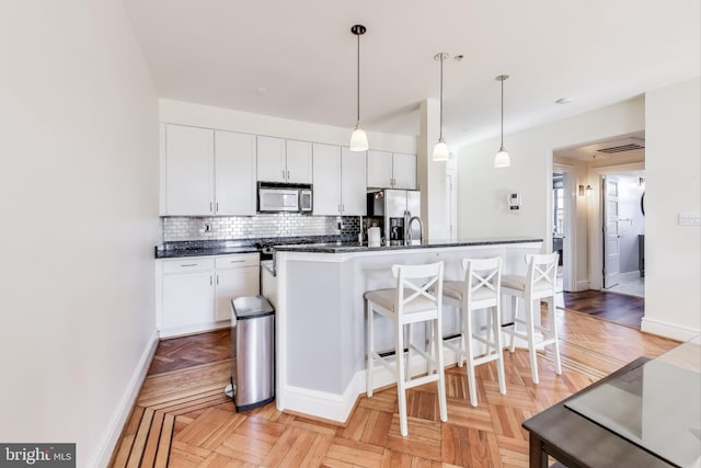 kitchen with stainless steel appliances, tasteful backsplash, pendant lighting, light parquet flooring, and white cabinets