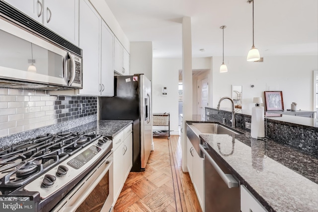 kitchen featuring white cabinetry, stainless steel appliances, decorative backsplash, decorative light fixtures, and dark stone counters