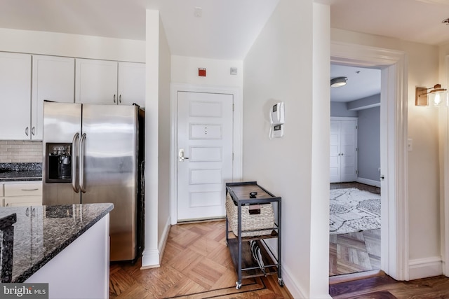 kitchen with tasteful backsplash, stainless steel fridge with ice dispenser, dark stone countertops, dark parquet floors, and white cabinets