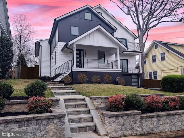 view of front of house featuring covered porch, board and batten siding, a front yard, fence, and stairs