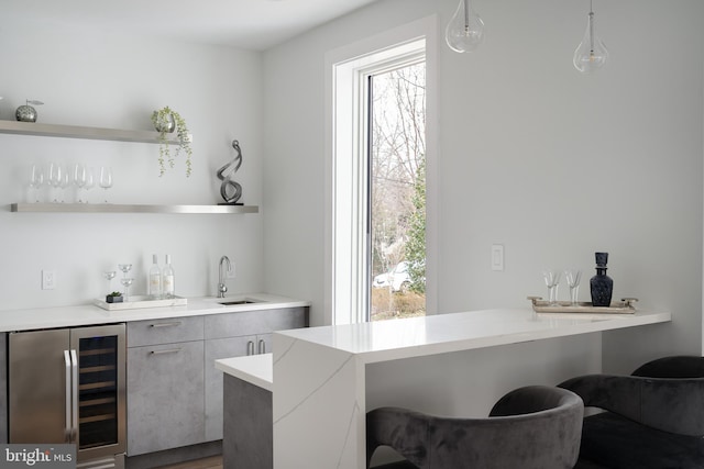 bar with beverage cooler, a sink, decorative light fixtures, and wet bar