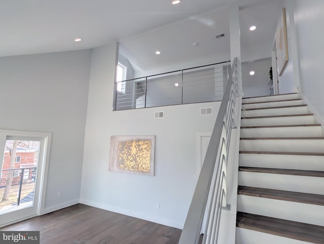 stairs featuring a high ceiling, wood finished floors, visible vents, and baseboards