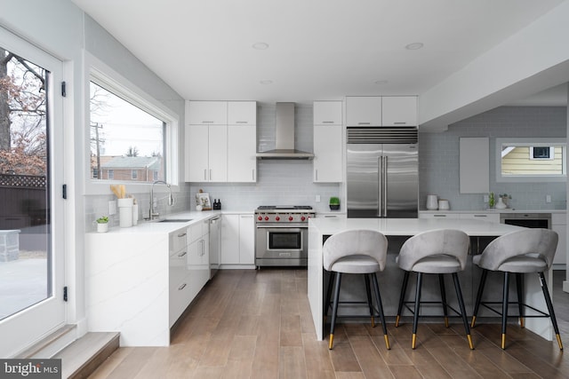 kitchen with a sink, white cabinetry, wall chimney range hood, tasteful backsplash, and high end appliances