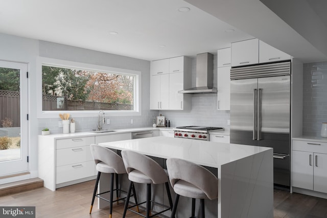 kitchen with wall chimney exhaust hood, appliances with stainless steel finishes, a center island, white cabinetry, and a sink