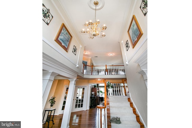 foyer featuring ornamental molding, wood finished floors, stairway, a towering ceiling, and ornate columns