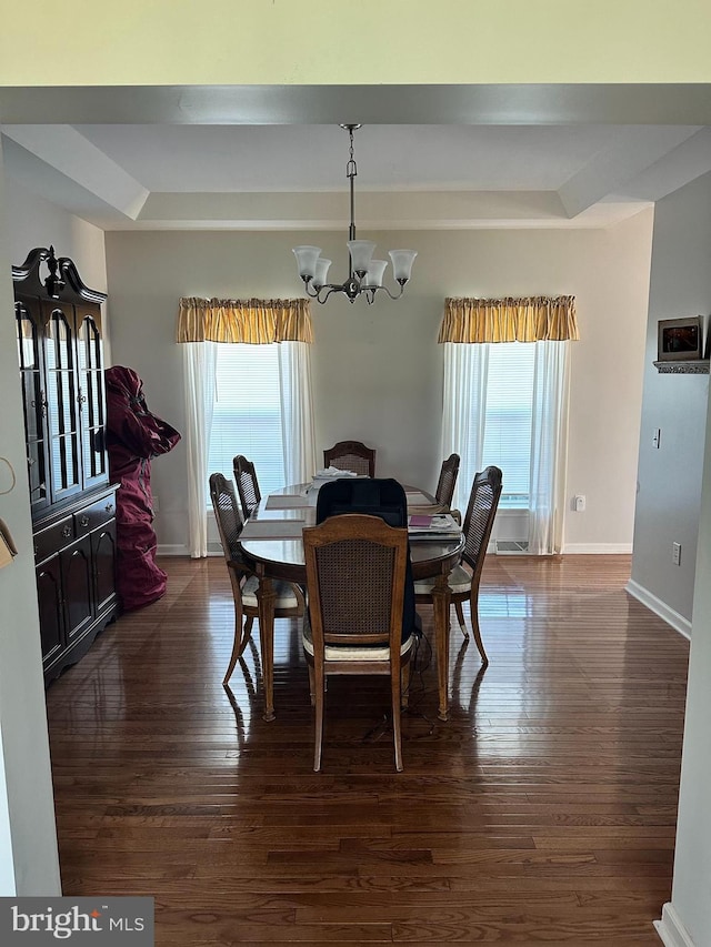 dining room with a raised ceiling, an inviting chandelier, and dark wood-type flooring