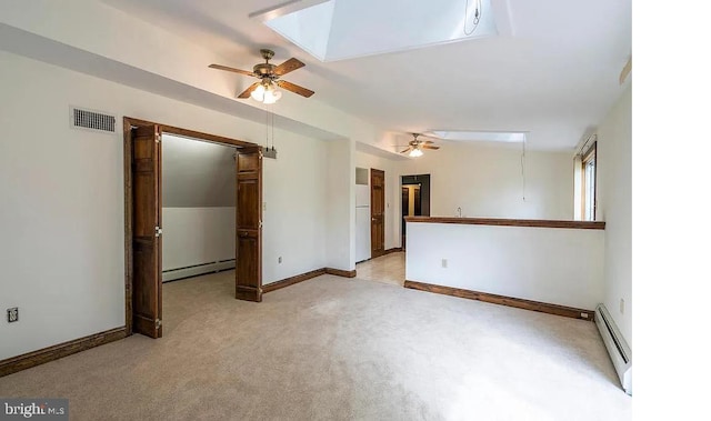 spare room with a skylight, light colored carpet, baseboard heating, and ceiling fan