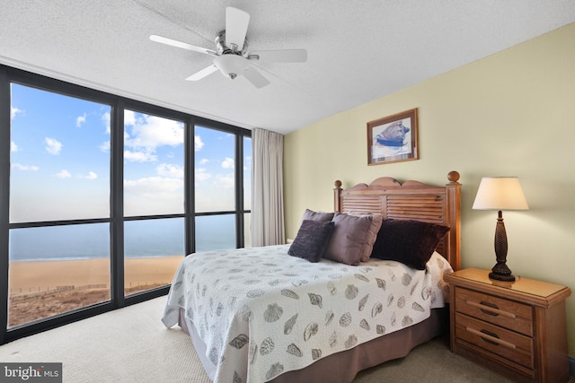 carpeted bedroom featuring ceiling fan, a water view, a wall of windows, and a textured ceiling