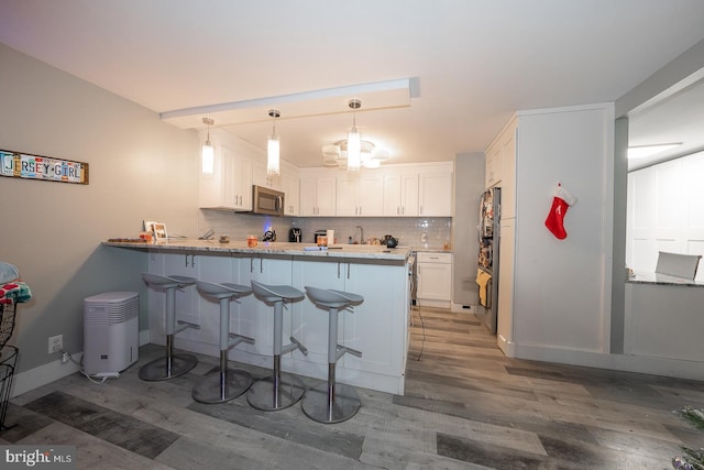 kitchen with white cabinetry, tasteful backsplash, kitchen peninsula, a breakfast bar area, and appliances with stainless steel finishes