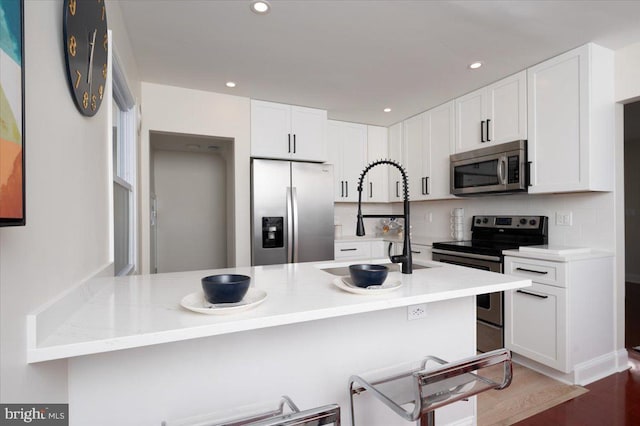 kitchen with light stone countertops, a breakfast bar, stainless steel appliances, sink, and white cabinetry