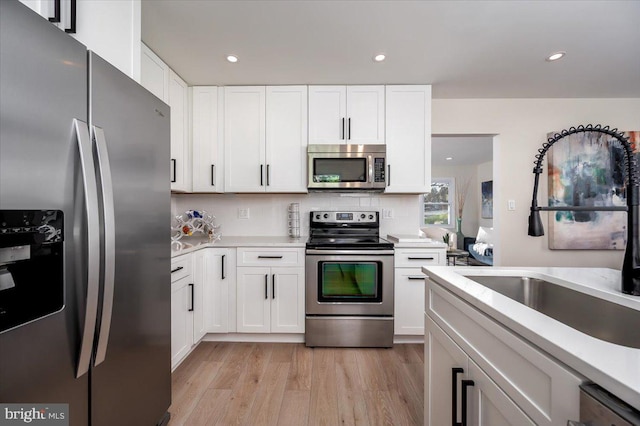 kitchen with white cabinets, stainless steel appliances, light hardwood / wood-style flooring, and sink