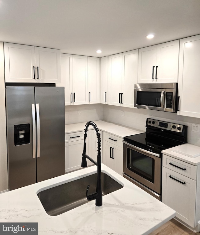 kitchen with backsplash, sink, appliances with stainless steel finishes, light stone counters, and white cabinetry