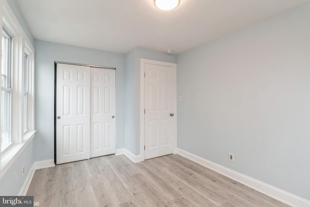 unfurnished bedroom with a closet, light hardwood / wood-style flooring, and multiple windows