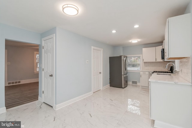 kitchen with sink, decorative backsplash, light stone countertops, white cabinetry, and stainless steel refrigerator