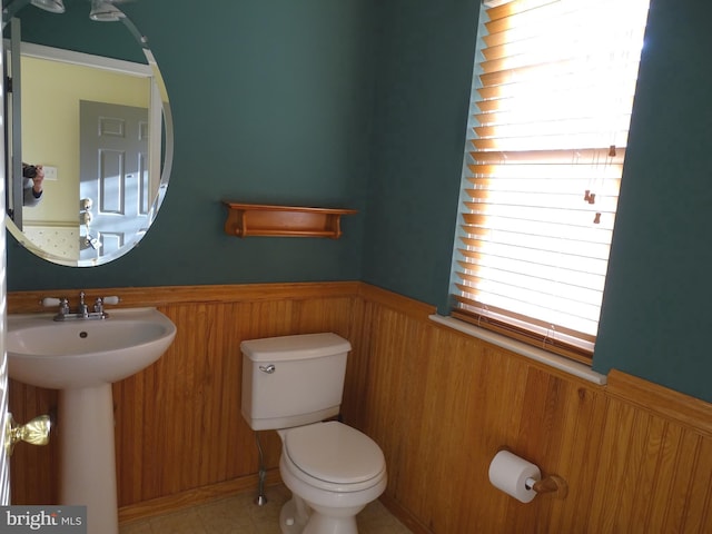 bathroom with tile patterned floors, wooden walls, sink, and toilet