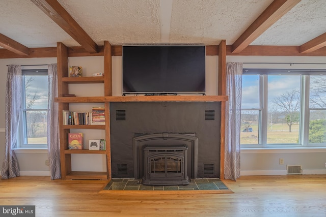 interior details with beamed ceiling, wood-type flooring, a wood stove, and a textured ceiling