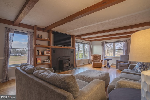 living room featuring a wood stove, beamed ceiling, light hardwood / wood-style floors, and a textured ceiling