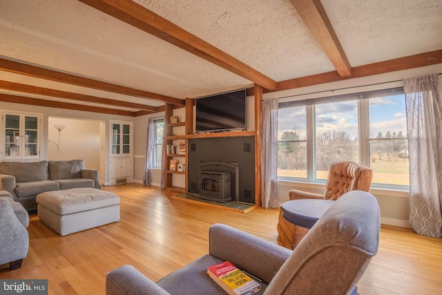 living room with a wood stove, beamed ceiling, plenty of natural light, a textured ceiling, and light wood-type flooring