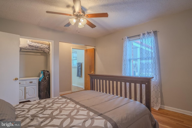 bedroom with a textured ceiling, light hardwood / wood-style flooring, a closet, and ceiling fan