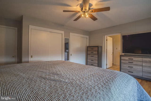 unfurnished bedroom featuring a textured ceiling, ceiling fan, light hardwood / wood-style floors, and two closets