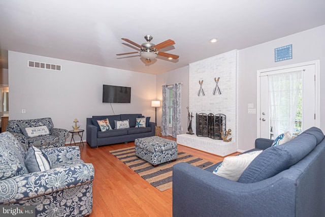 living room with ceiling fan, wood-type flooring, and a brick fireplace