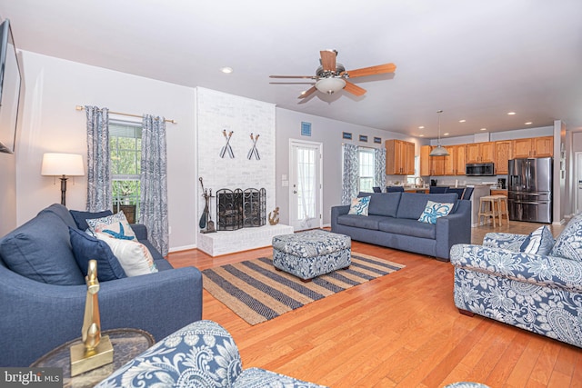 living room featuring a fireplace, light wood-type flooring, and ceiling fan