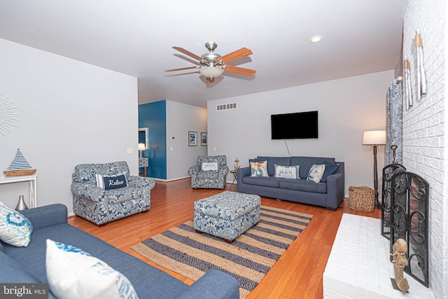 living room with a fireplace, wood-type flooring, and ceiling fan