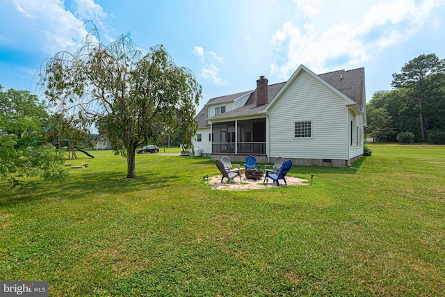 rear view of property featuring a sunroom, an outdoor fire pit, and a lawn