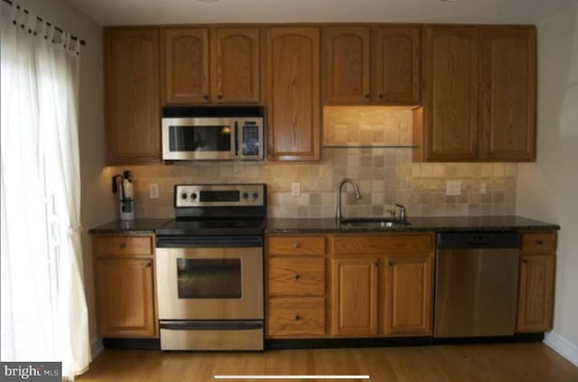 kitchen featuring sink, stainless steel appliances, dark stone counters, and light hardwood / wood-style flooring