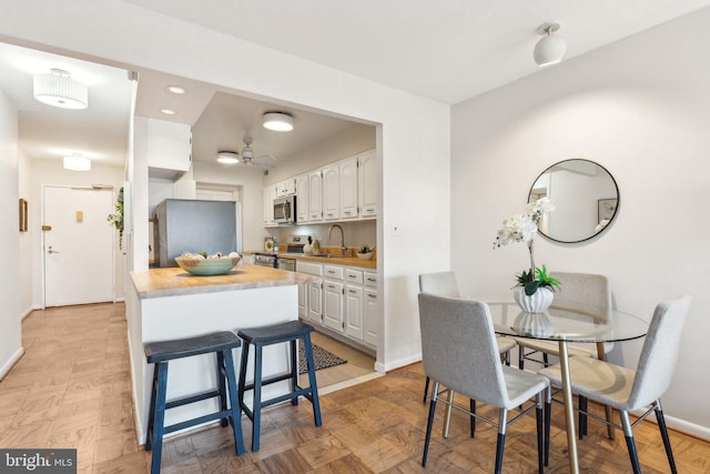 kitchen with wooden counters, a kitchen breakfast bar, sink, white cabinetry, and stainless steel appliances