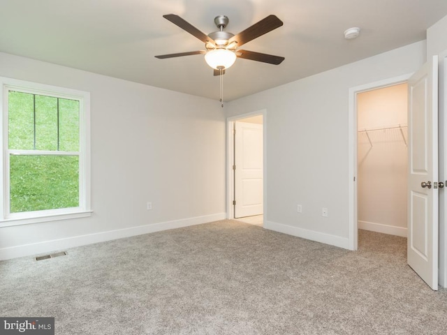 unfurnished bedroom with multiple windows, light carpet, ceiling fan, and a spacious closet