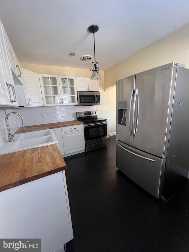 kitchen with stainless steel appliances, sink, white cabinetry, hanging light fixtures, and butcher block counters