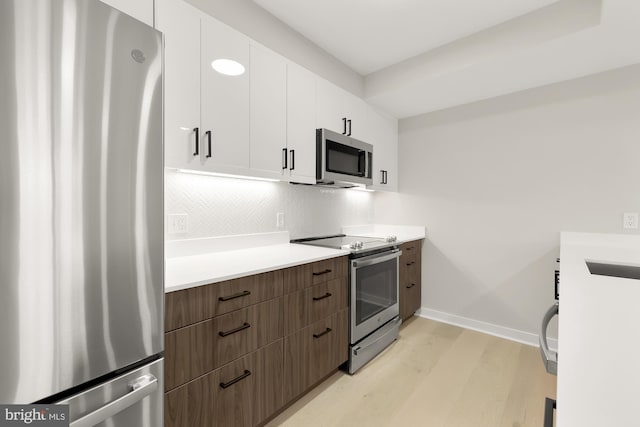 kitchen featuring appliances with stainless steel finishes, tasteful backsplash, dark brown cabinetry, light hardwood / wood-style flooring, and white cabinets