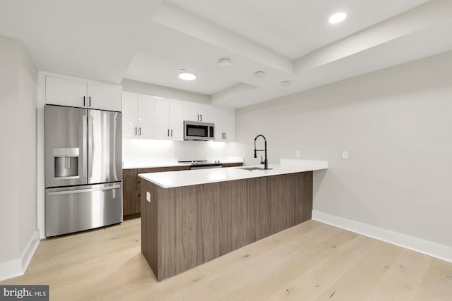 kitchen with appliances with stainless steel finishes, a tray ceiling, sink, light hardwood / wood-style floors, and white cabinetry