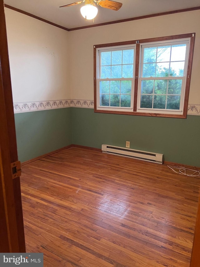 empty room featuring ceiling fan, hardwood / wood-style floors, ornamental molding, and a baseboard heating unit