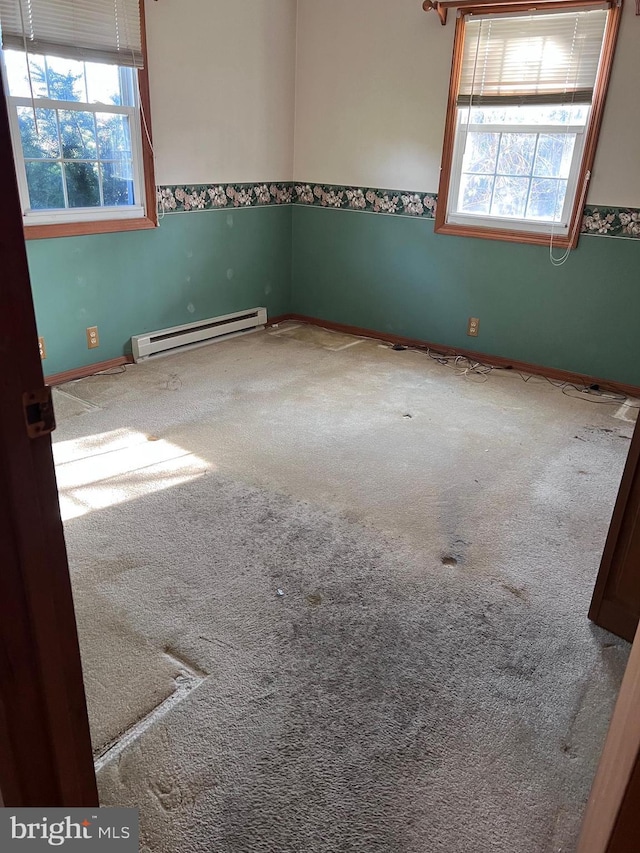 empty room featuring carpet flooring, plenty of natural light, and a baseboard heating unit