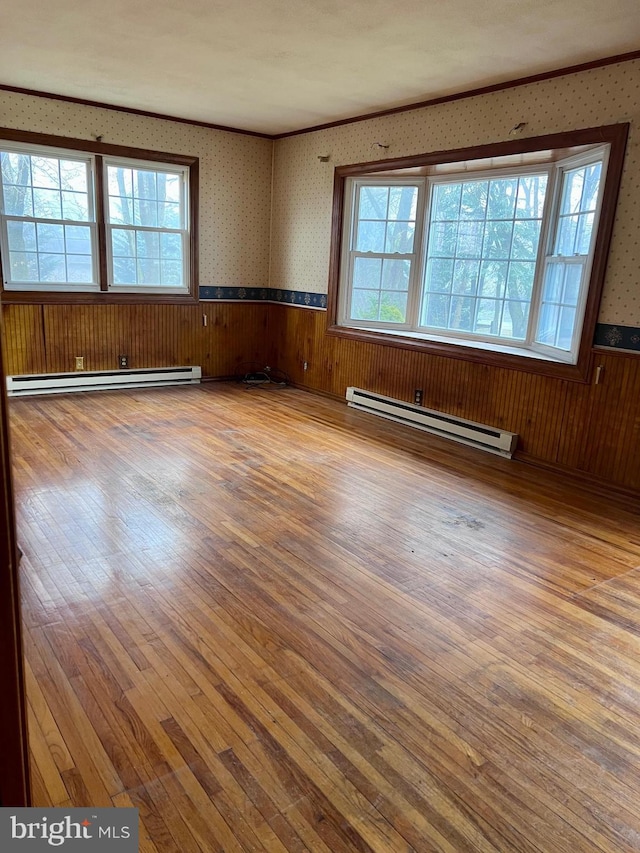 unfurnished room featuring wood walls, wood-type flooring, and a baseboard radiator