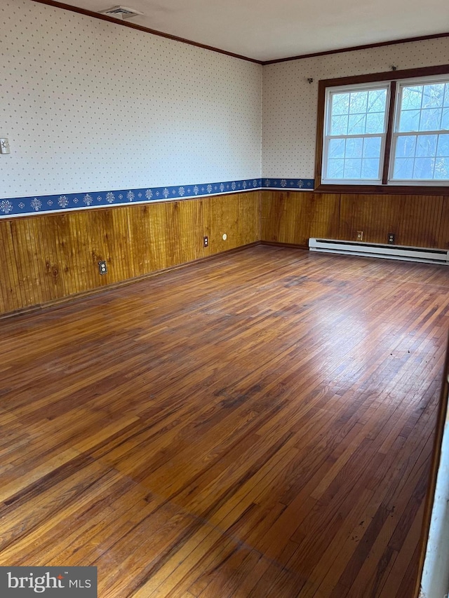 empty room with dark hardwood / wood-style floors, wood walls, baseboard heating, and crown molding