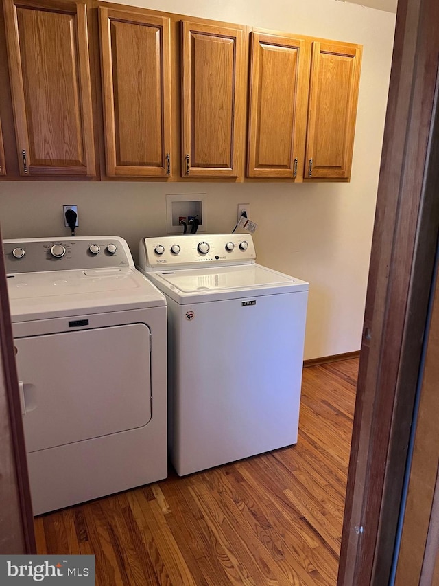 clothes washing area featuring washing machine and clothes dryer, cabinets, and wood-type flooring